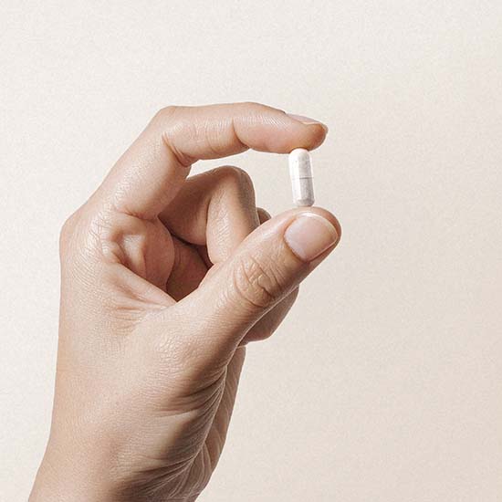 Eine Hand hält zwischen den Fingern eine Kapsel