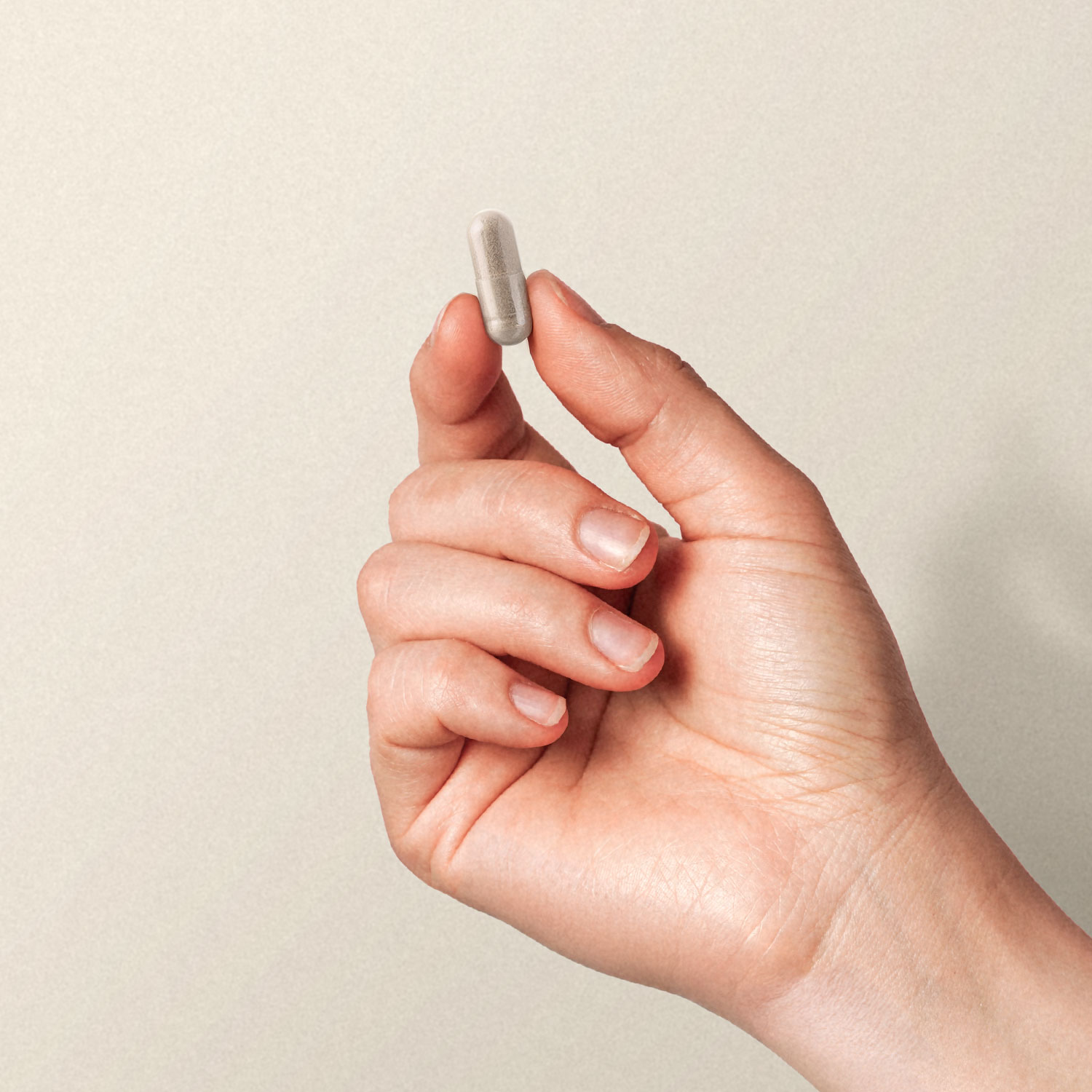 Eine Hand hält eine kleine Kapsel zwischen Daumen und Zeigefinger