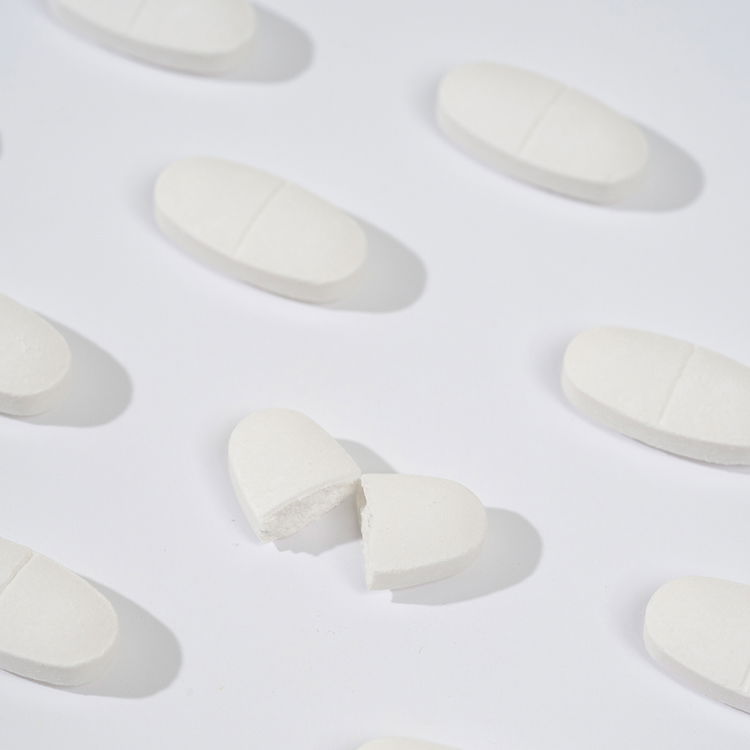 Mehrere weiße Tabletten auf weißem Hintergrund, eine davon gebrochen