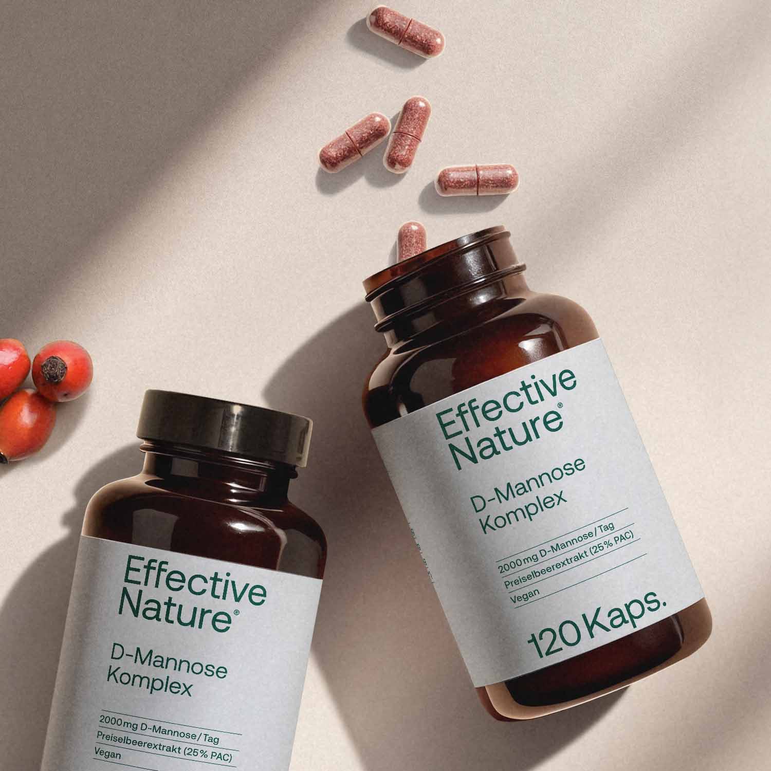 Zwei Flaschen mit Effective Nature D-Mannose Komplex Kapseln, umgeben von Preiselbeeren.