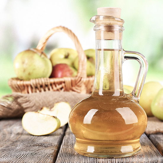 Eine Flasche Apfelessig auf einem Holztisch vor einem Apfelkorb