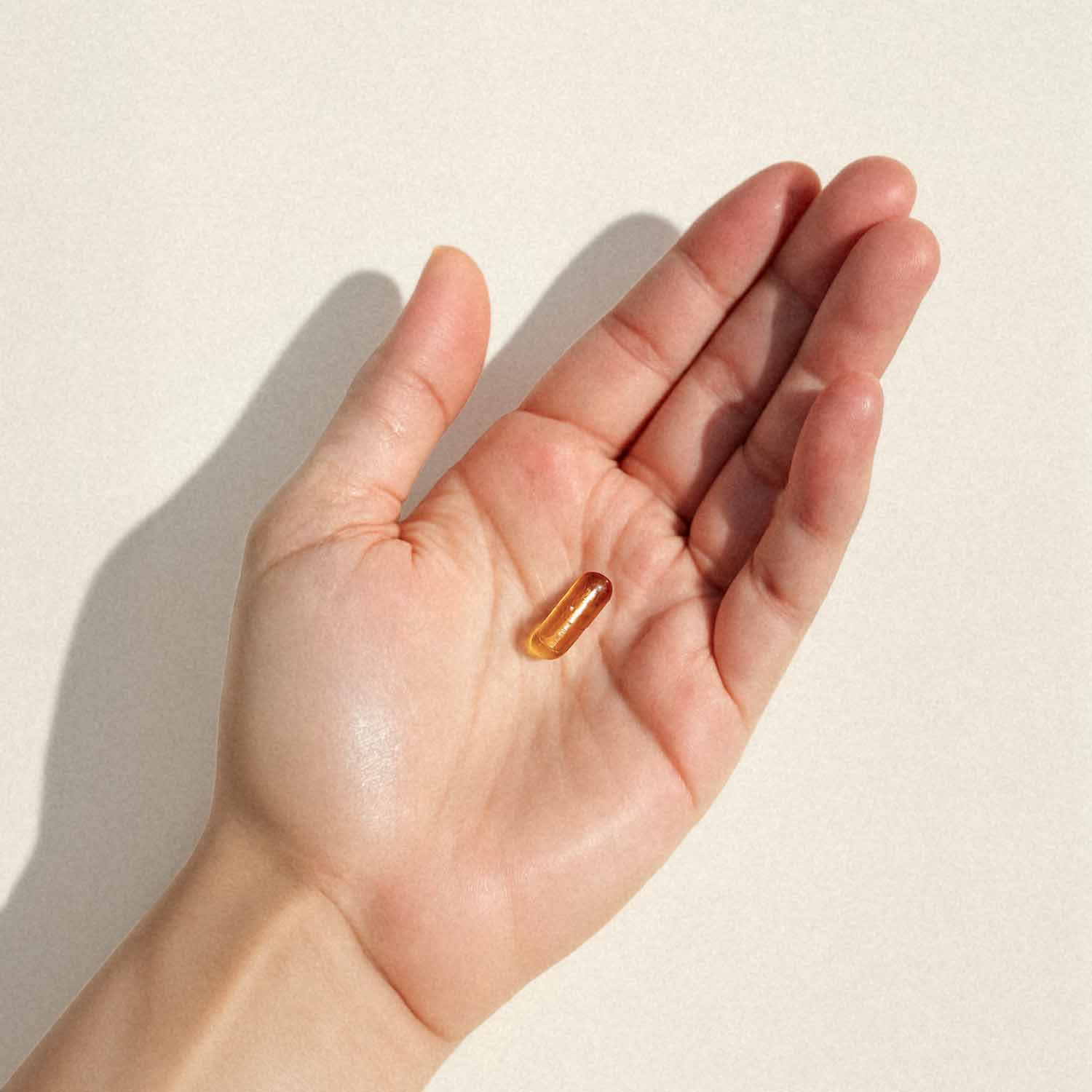 Close-up einer Hand, die eine kleine, transparente Kapsel auf einer offenen Handfläche hält, vor einem hellen Hintergrund.