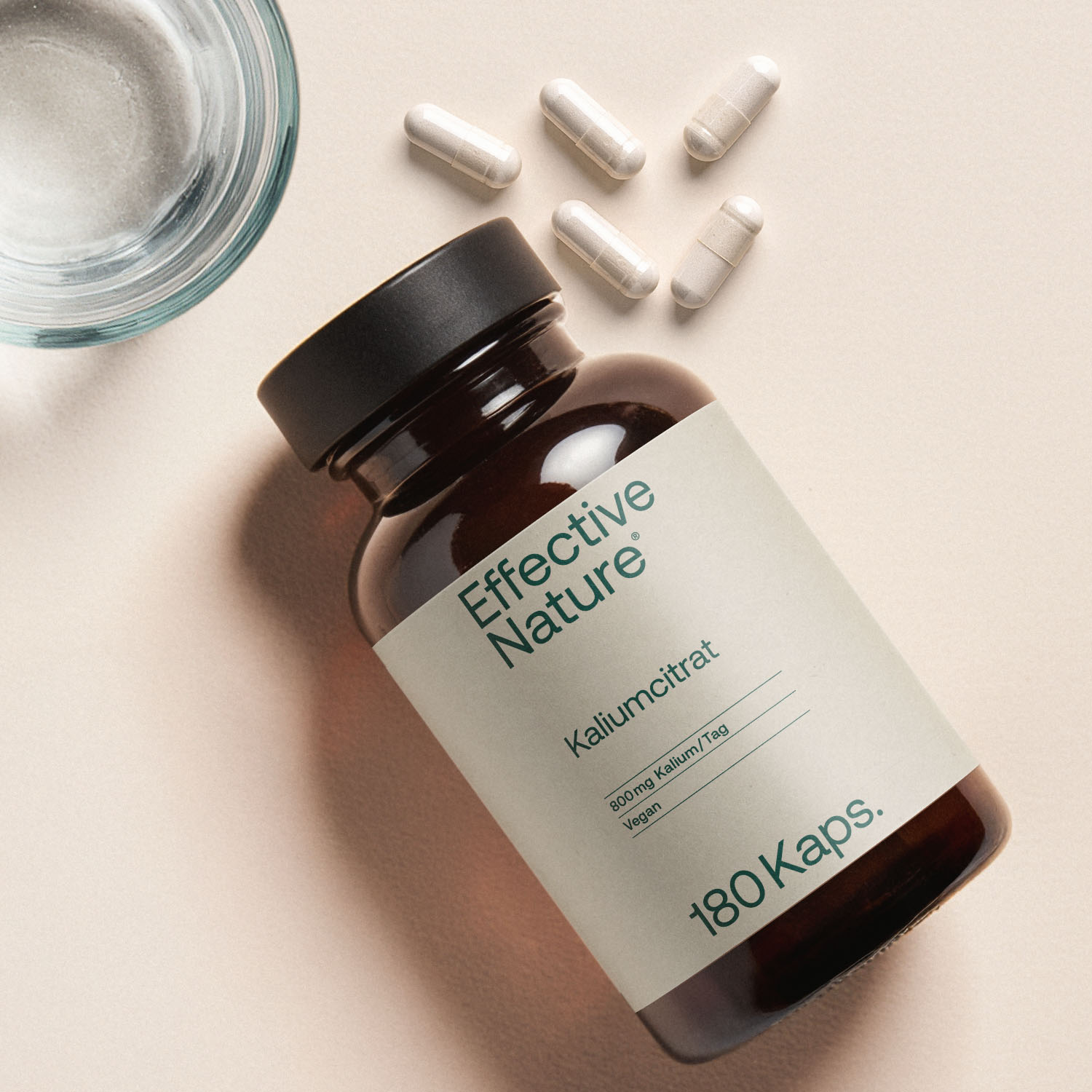 Nahaufnahme einer Glasflasche mit Kaliumcitrat-Kapseln von Effective Nature und einigen losen Kapseln daneben