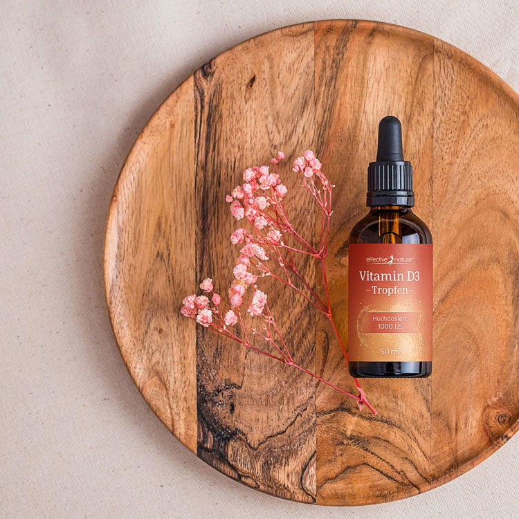Flasche Vitamin D3 Tropfen auf einem runden Holzteller mit rosa getrockneten Blumen