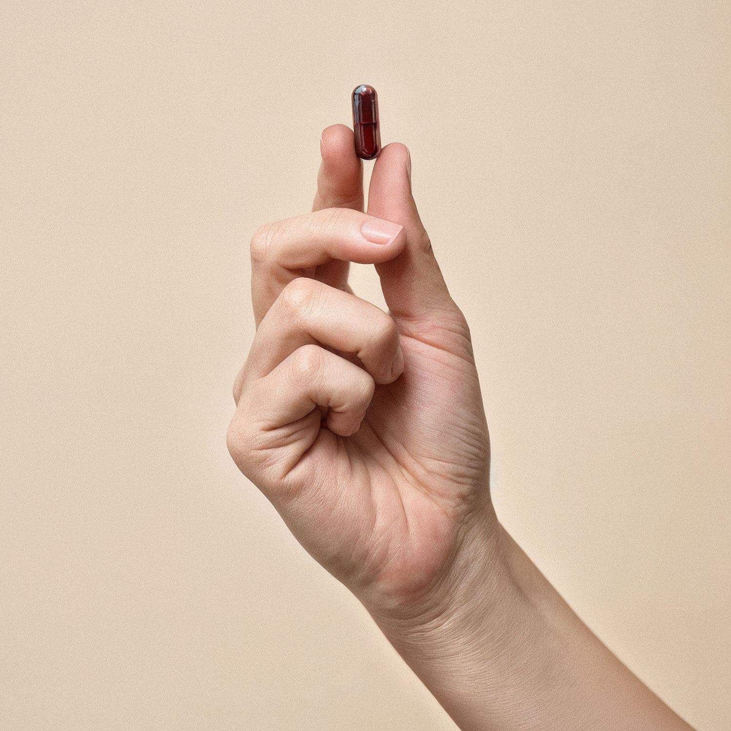 Hand hält eine kleine rote Pille vor neutralem Hintergrund