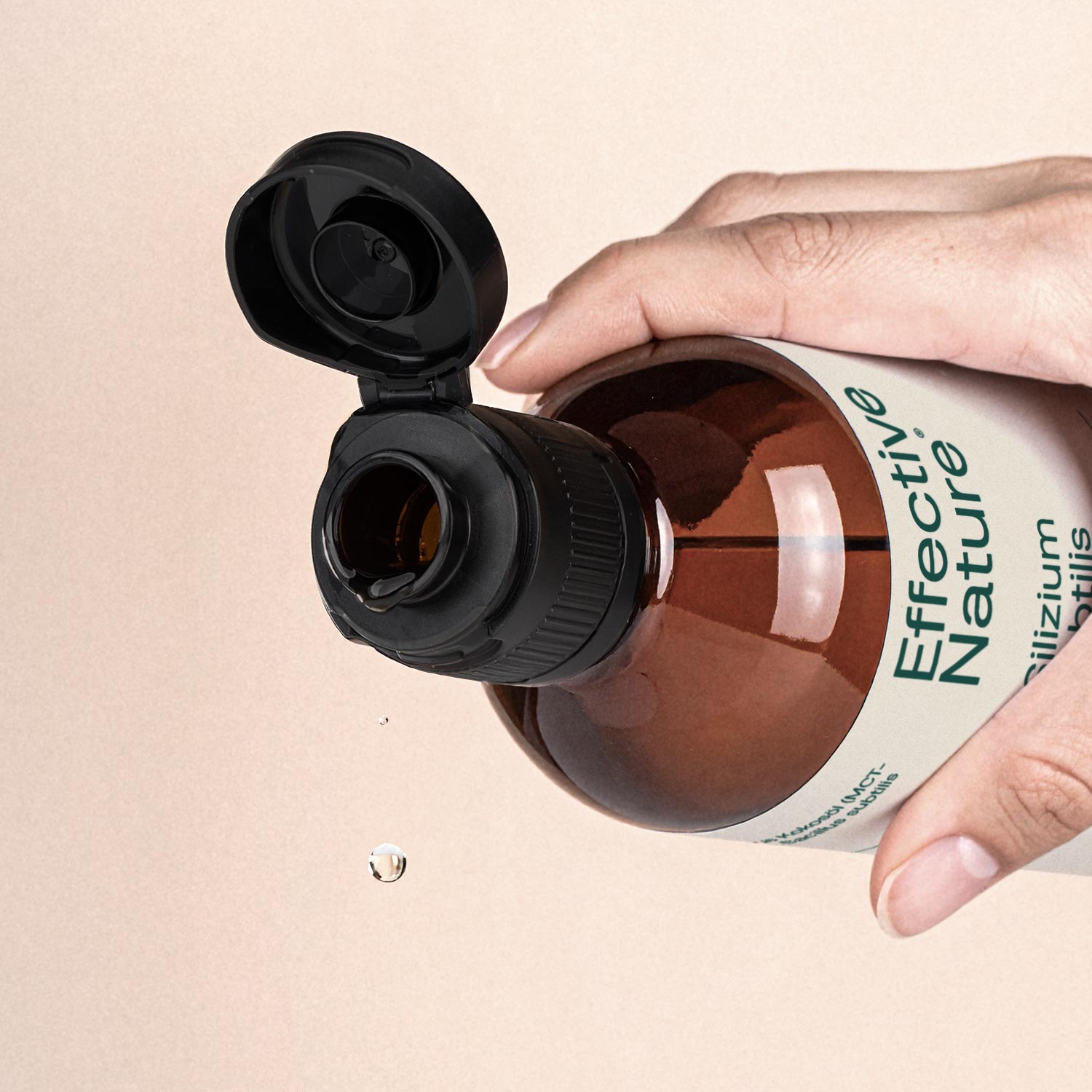 Nahaufnahme einer braunen Flasche von Effective Nature mit offenem Tropfverschluss, gehalten von einer Hand, mit herabfallendem Tropfen