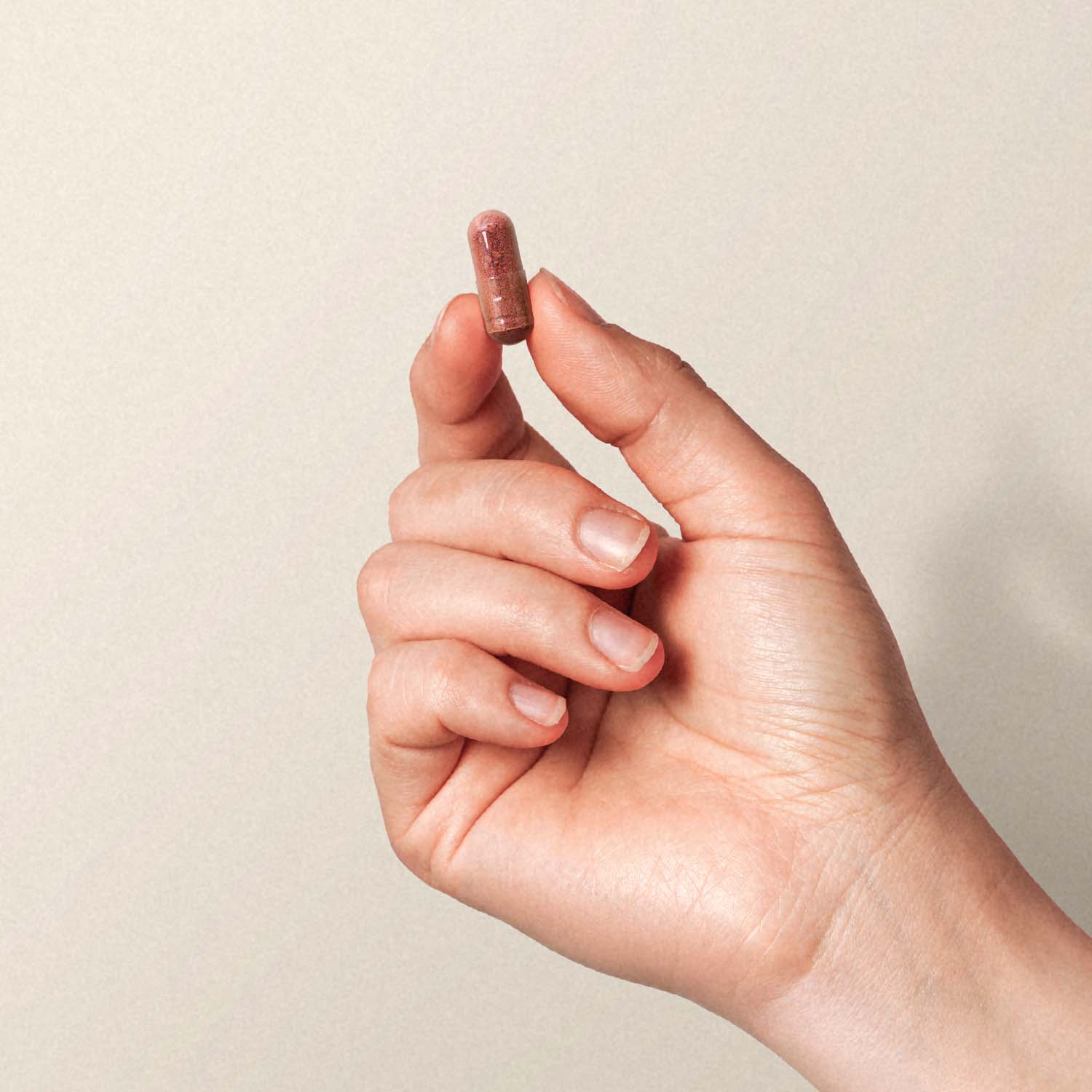 Hand hält eine kleine braune Kapsel zwischen Daumen und Zeigefinger vor neutralem Hintergrund