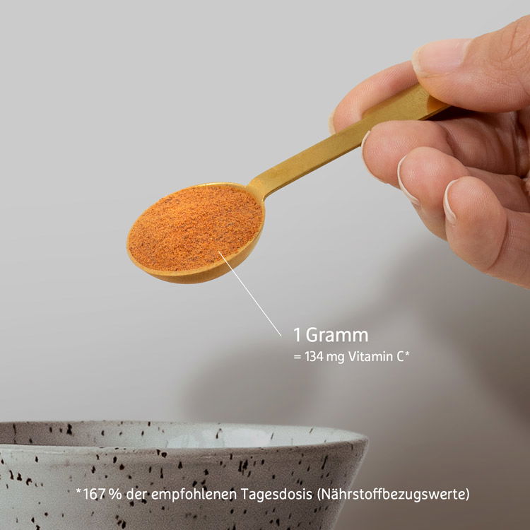 Hand hält einen Löffel mit Vitamin C Pulver über einer Schale; 1 Gramm enthält 134 mg Vitamin C