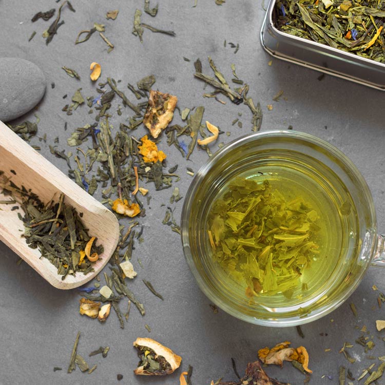 Eine Tasse grüner Tee mit losen Blättern, getrockneten Blumen und Früchten auf einem Tisch