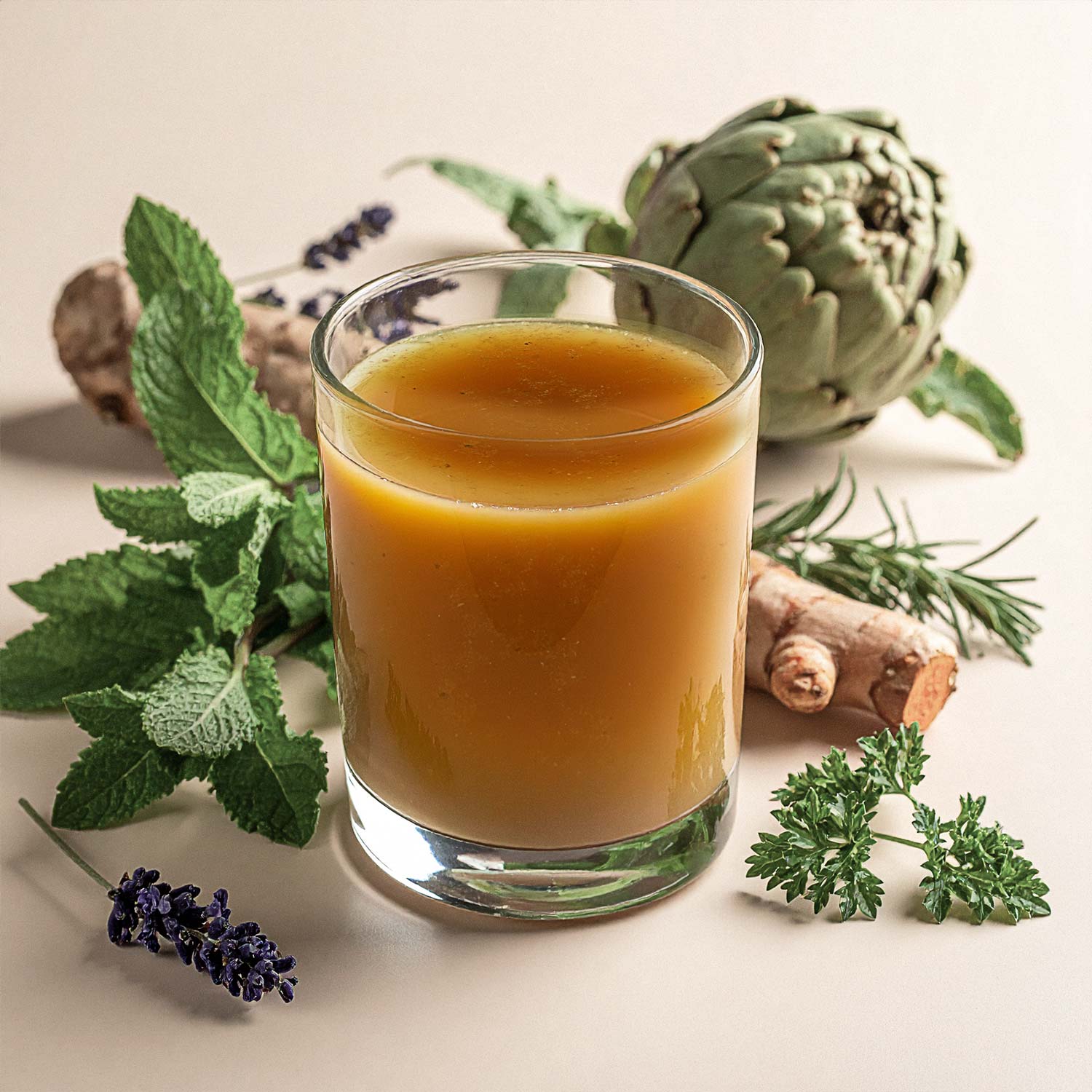 Ein Glas mit orangefarbenem Kräutersaft, umgeben von frischen Kräutern und einer Artischocke