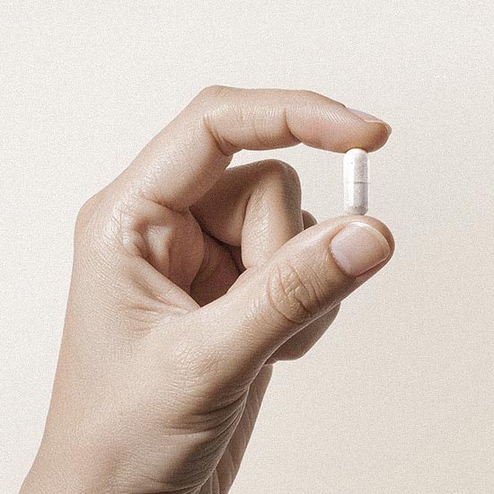 Hand mit einer Kapsel zwischen den Fingern