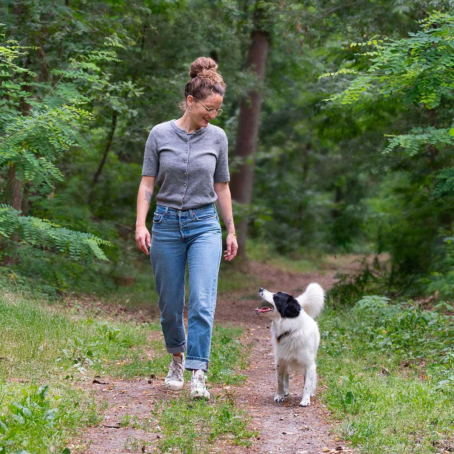 Frau geht lächelnd mit ihrem Hund auf einem Waldweg spazieren