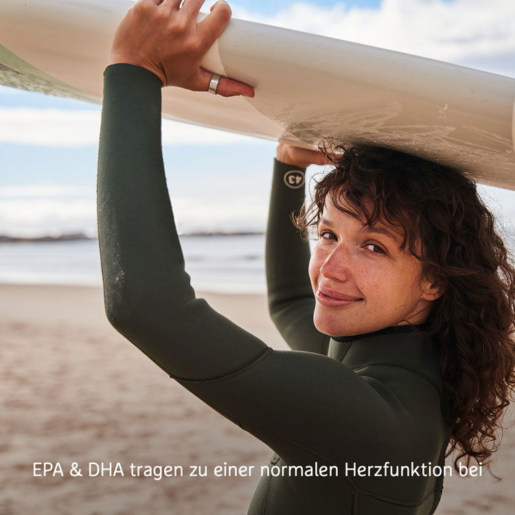 Eine Frau am Strand trägt ein Surfbrett