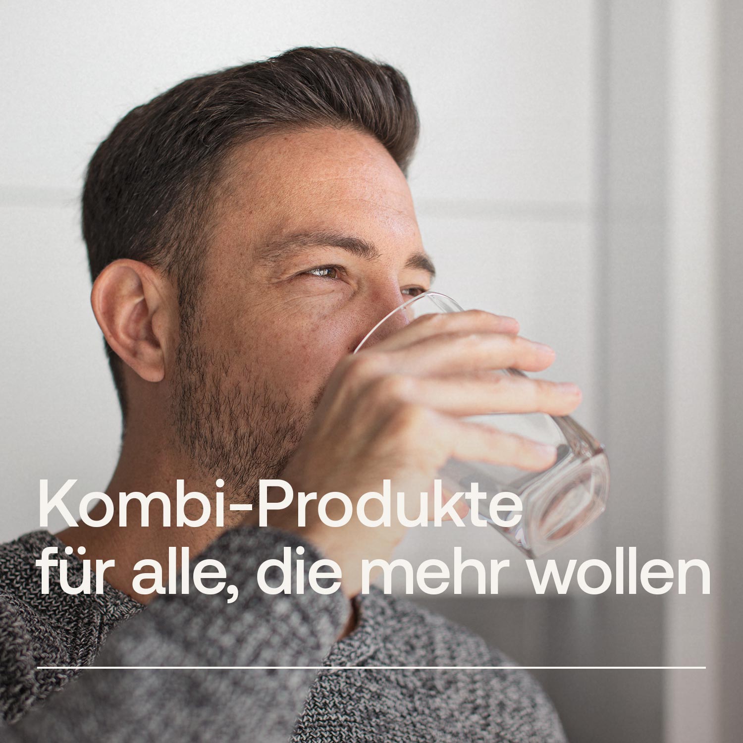 Mann in grauem Pullover trinkt Wasser aus einem Glas vor hellem Hintergrund