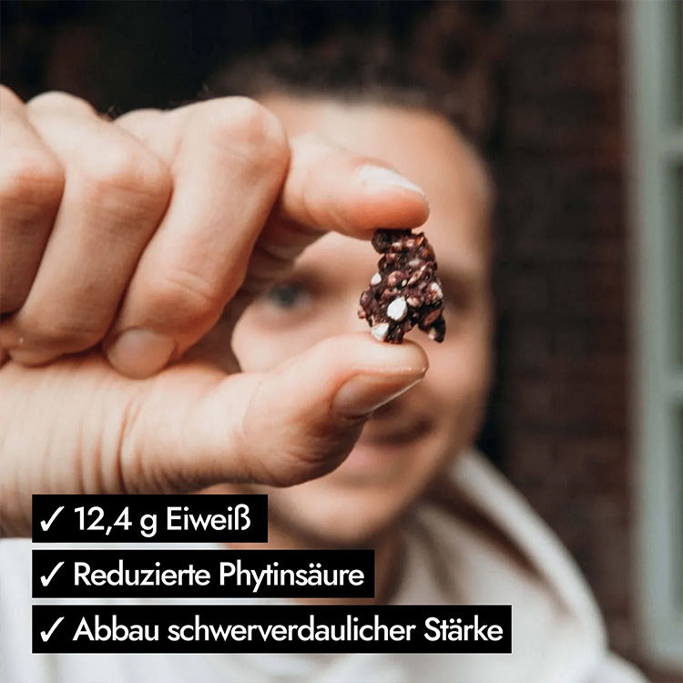 Person hält einen snackgroßen, gekeimten Proteinriegel mit Text: 12,4 g Eiweiß, reduzierte Phytinsäure, Abbau schwerverdaulicher Stärke.