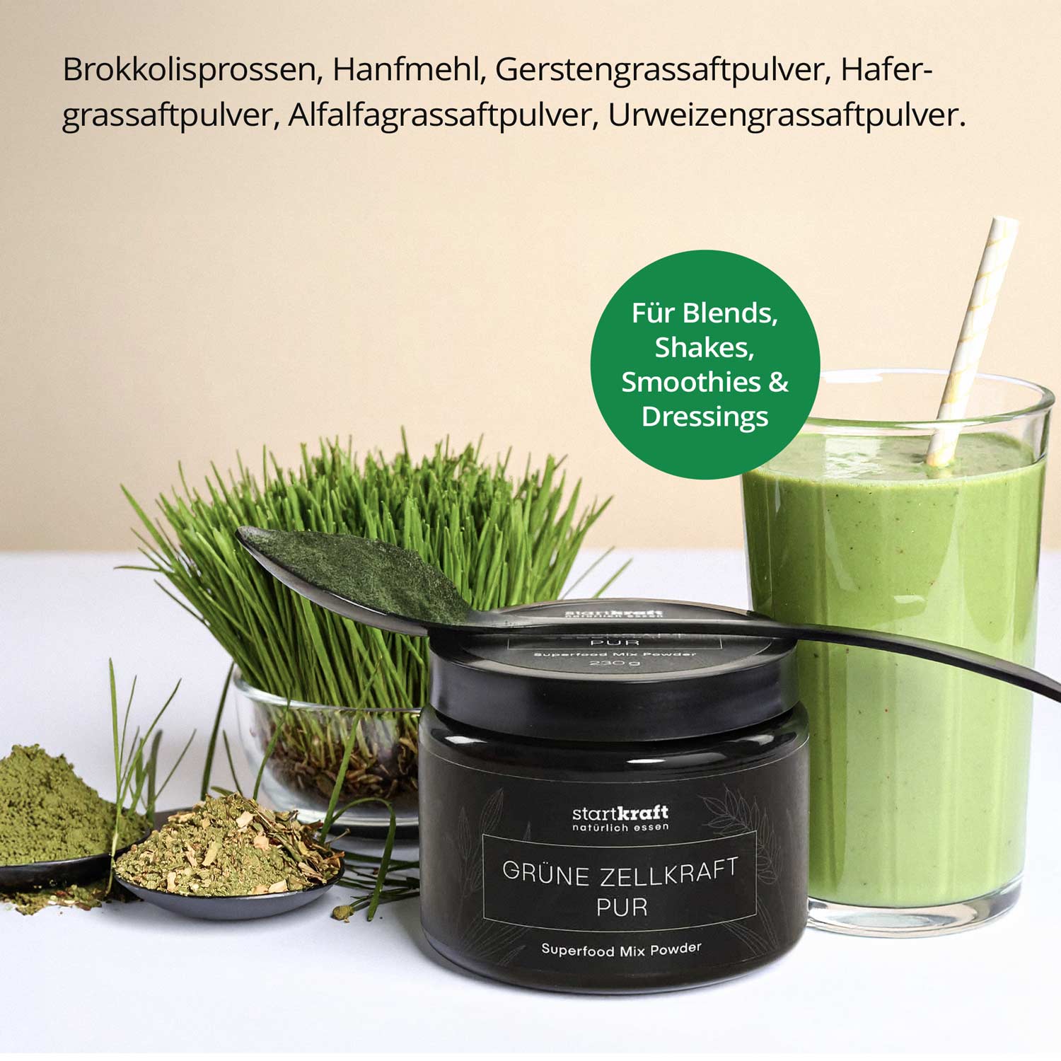 Ein Glas grüner Smoothie neben einer Dose Startkraft Grüne Zellkraft Pur Superfood Mix Pulver, umgeben von Gräsern und Pulverzutaten, ideal für gesunde Shakes und Dressings.