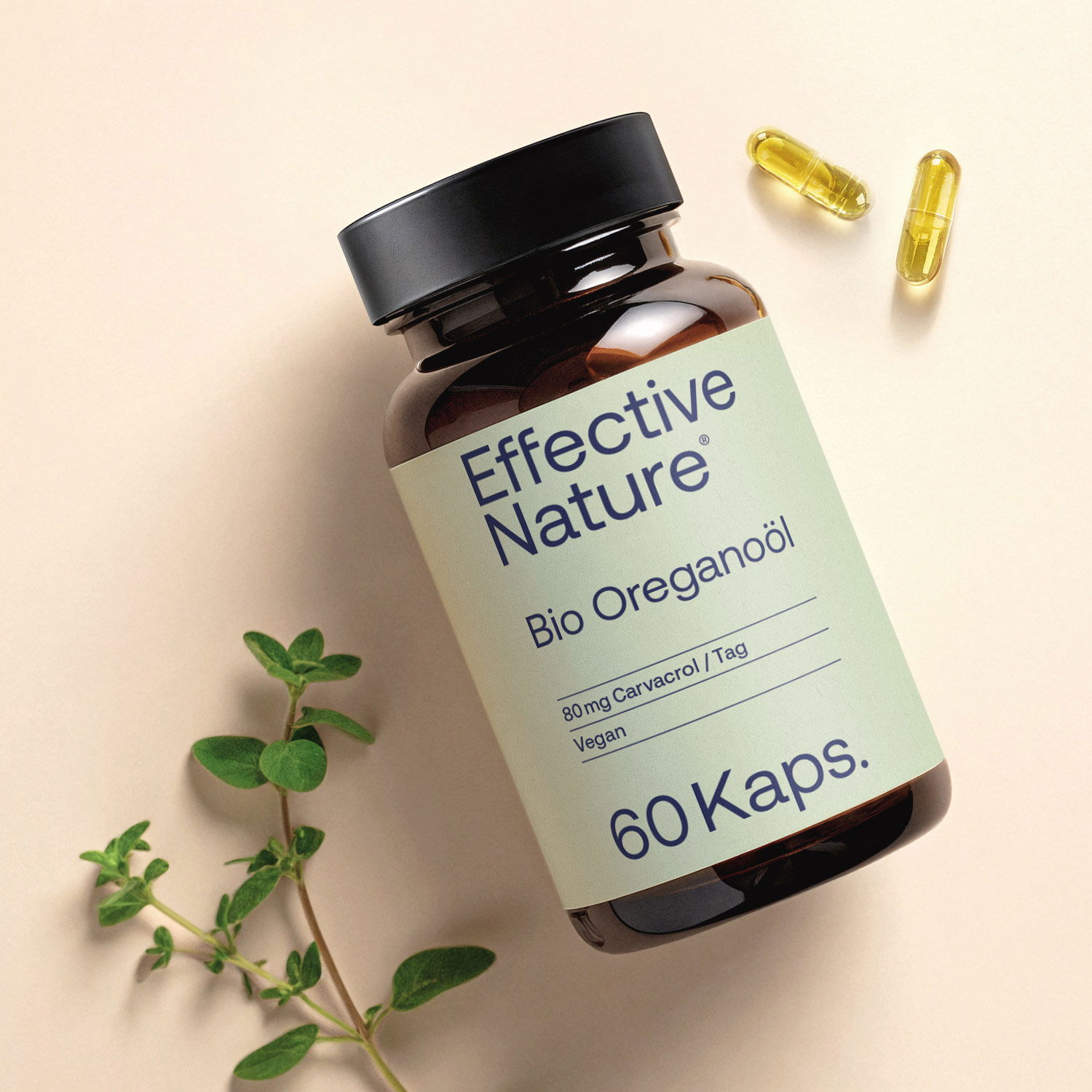 Flasche mit Bio Oreganoöl Kapseln von Effective Nature und zwei Kapseln auf hellem Hintergrund neben einem Oreganozweig
