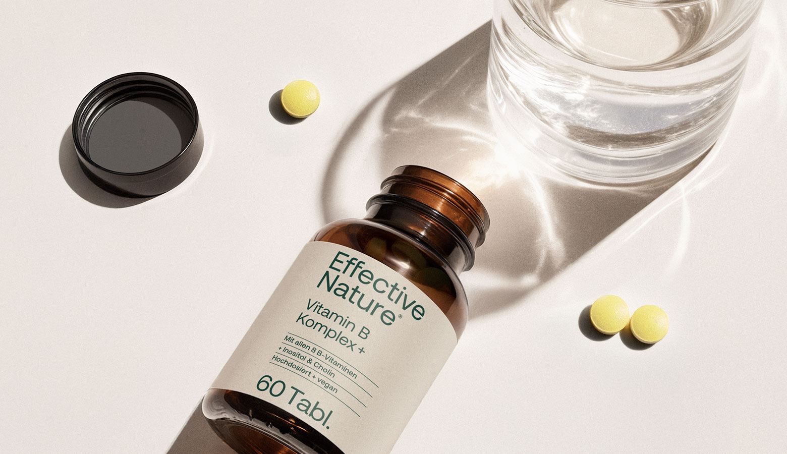 Eine Dose Vitamin B Komplex+ liegt neben einem Glas Wasser auf einem Tisch