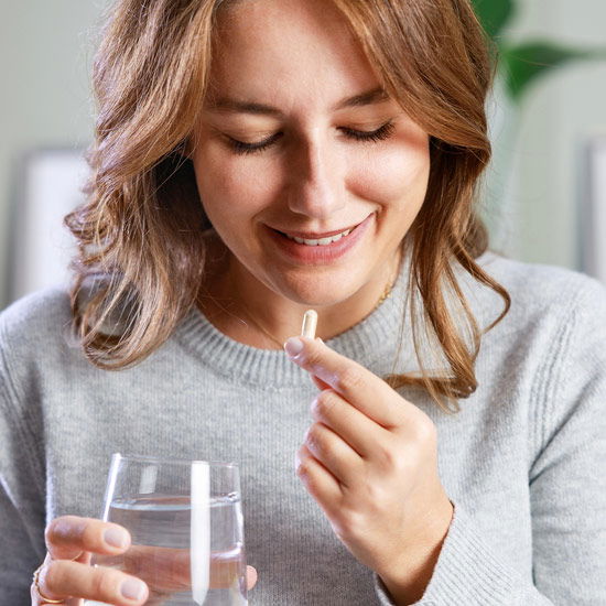 Frau nimmt Kapsel mit einem Glas Wasser ein