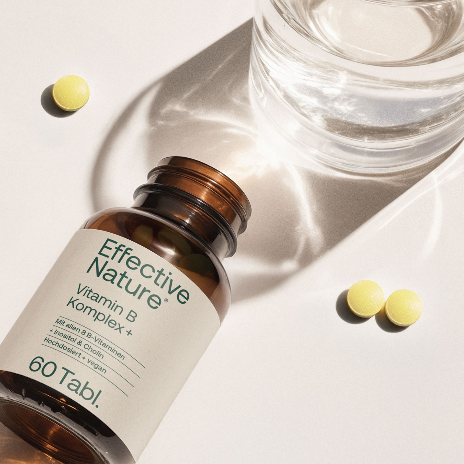 Flasche von Effective Nature Vitamin B Komplex+ mit zwei gelben Tabletten und einem Glas Wasser
