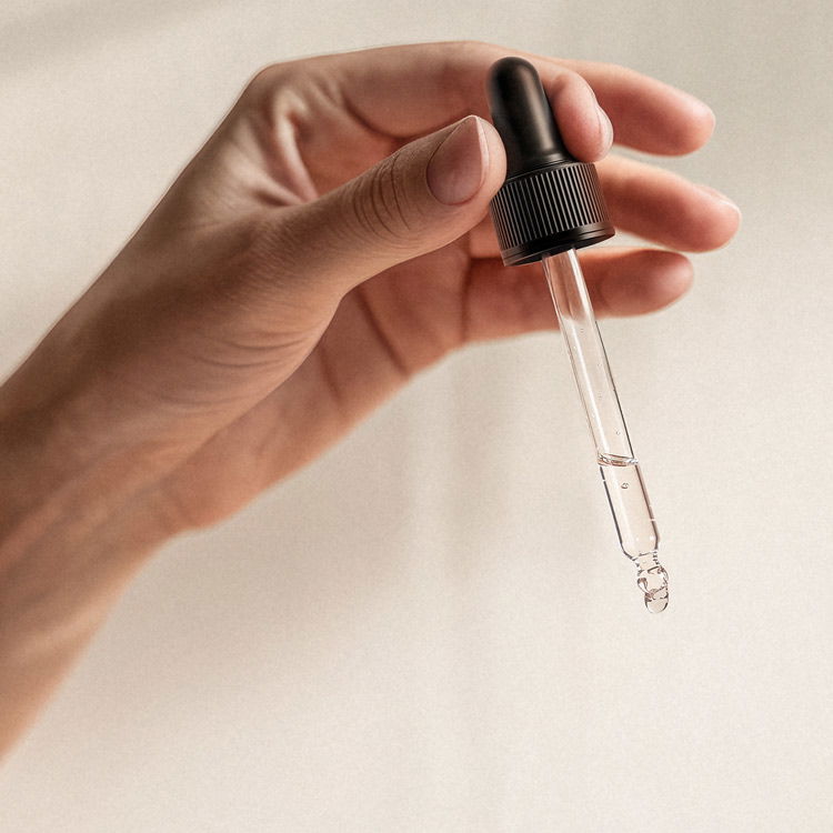 Nahaufnahme einer Hand, die eine Pipette mit transparentem Serum hält, ideal für Hautpflegeprodukte