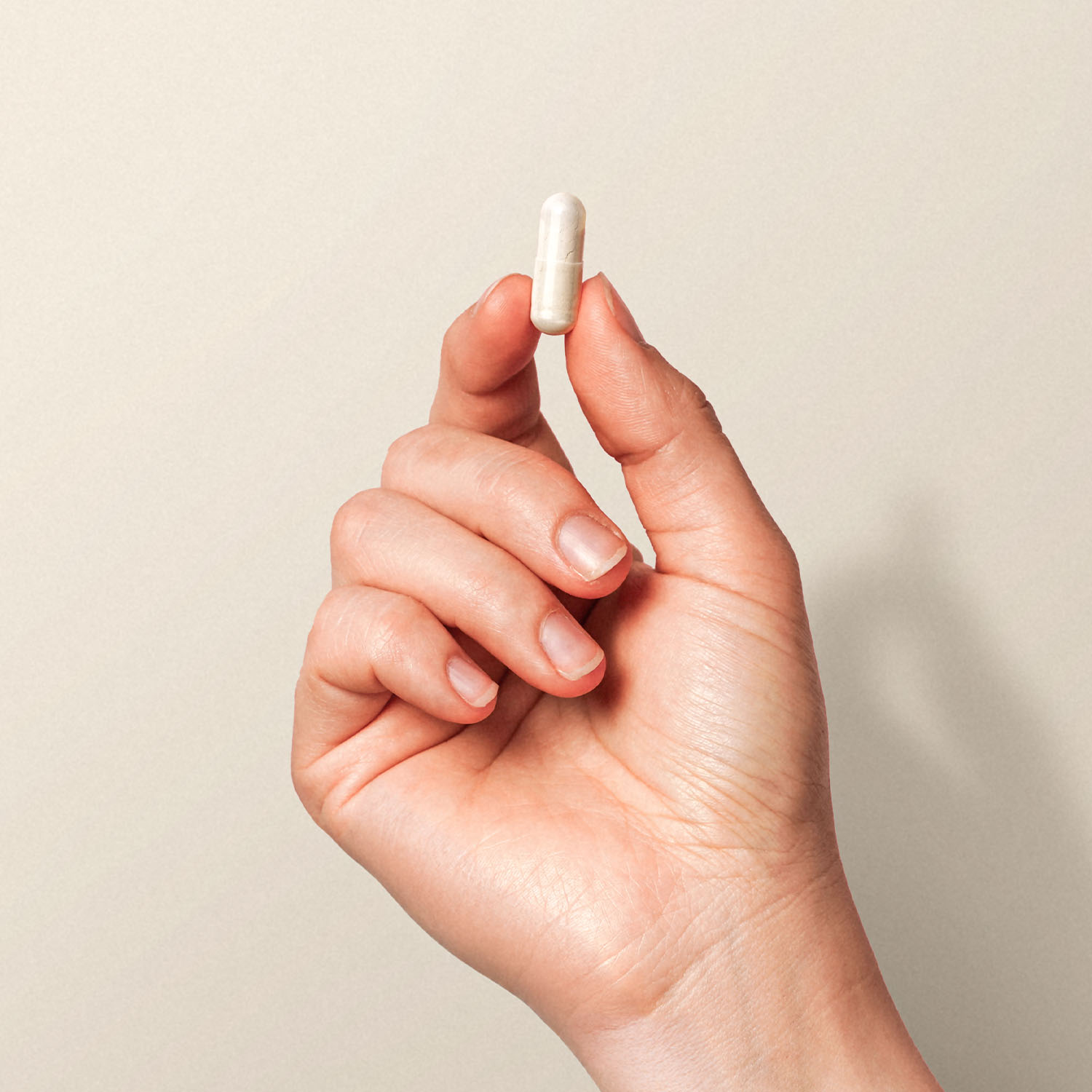 Nahaufnahme einer Hand, die eine weiße Kapsel zwischen Daumen und Zeigefinger hält