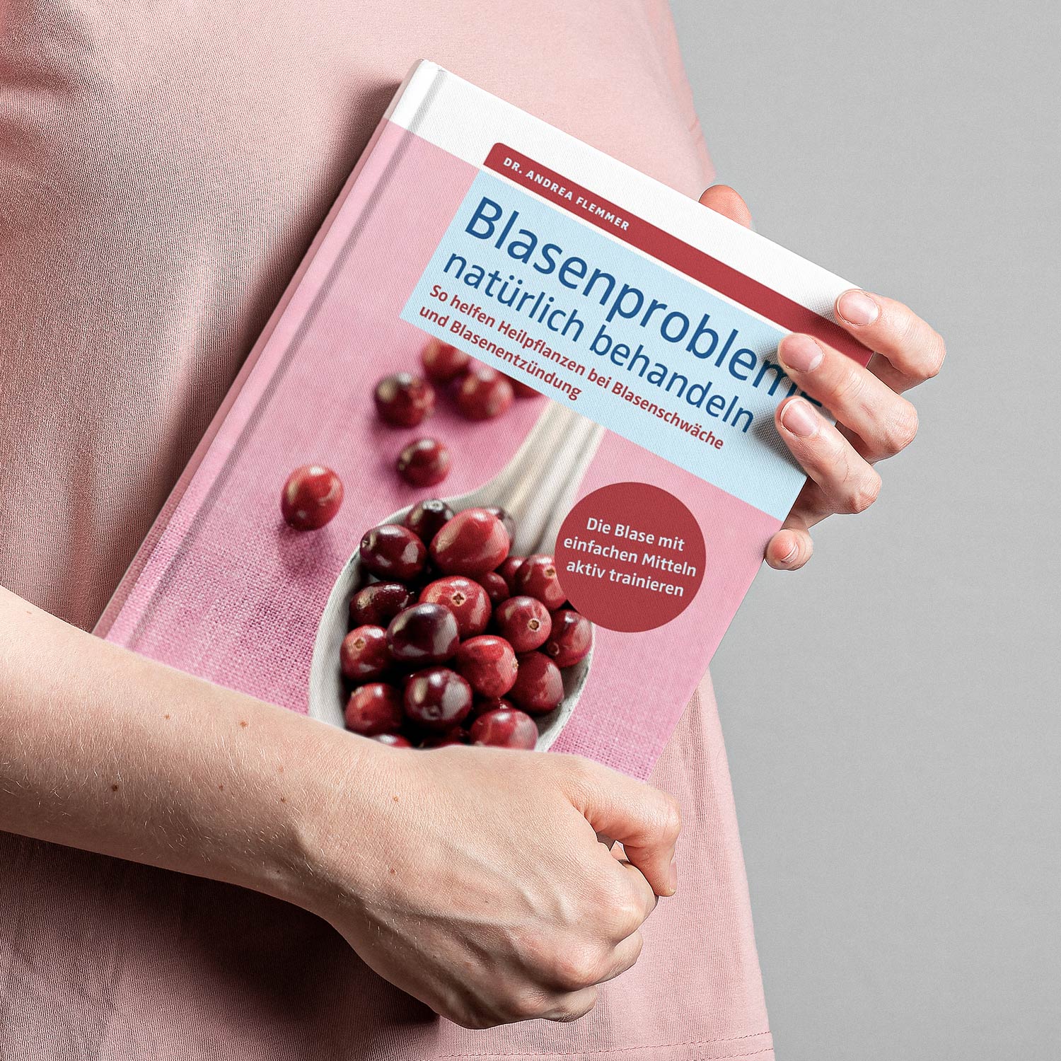Person hält Buch mit Titel 'Blasenprobleme natürlich behandeln', abgebildet sind auch Cranberries