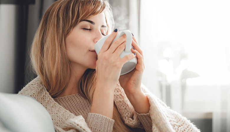 Frau auf Sofa mit Kaffeetasse in der Hand